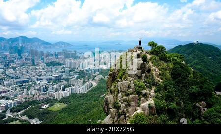 Luftaufnahme eines allein Reisenden Mädchens, das auf meinem Gipfel des felsigen Berges steht, mit Hong Kong Stadt und Hafen im Hintergrund. Stockfoto