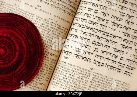 Eine alte jüdische Bibel und ein rot gestrickter jüdischer Ballen. Selektiver Fokus. Nahaufnahme des hebräischen Textes Stockfoto