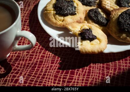 Gebissen Kekse mit Mohnfüllung und Kaffee bei Tageslicht, Backstube Hintergrund, Stockfoto