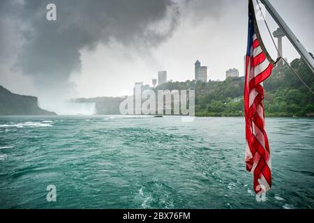 Flagge der Vereinigten Staaten mit den Niagarafällen im Hintergrund, bewölktem Tag und surrealer Atmosphäre Stockfoto