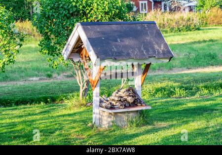 Dekorativer Holzbrunnen im Garten. Typisch rot gefärbte Holz schwedischen dekorativen Design für Garten auf dem Land Haus. Getrimmtes Gras vor Stockfoto