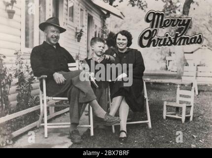 Eine Retro-Weihnachtskarte von einer Familie in Oregon, um 1948, die einen Mann, eine Frau und einen kleinen Jungen zeigt, der in ihrem Hof sitzt. Stockfoto