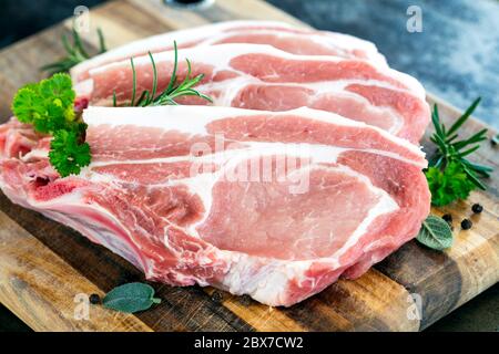 Rohe Schweinekoteletts auf dem Schneidebrett, mit frischen Kräutern und Gewürzen. Stockfoto