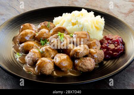 Schwedische Fleischbällchen mit Kartoffelpüree, Soße und Preiselbeere auf schwarzem Teller. Seitenansicht, über Schiefer. Stockfoto