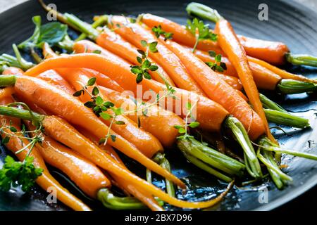 Gebratene gebutterte Babykarotten mit Kräutern auf schwarzem Teller. Stockfoto