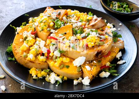 Salat aus geröstetem Butternusskürbis oder Kürbis, mit Mais und Chili Salsa, Feta-Käse und Pepitas. Mit Minze gekrönt. Stockfoto