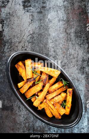 Süßkartoffel-Pommes in schwarzer Schüssel, Draufsicht über Schiefer. Stockfoto