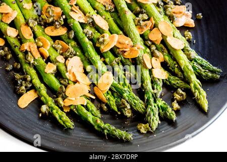 Gerösteter Spargel mit gerösteten Mandelflocken und Kapern. Schwarze Platte über Weiß. Stockfoto