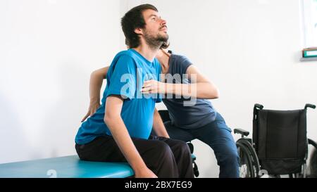 Physiotherapeut, der mit behinderten Menschen im Rollstuhl auf einem Therapietisch trainiert. Stockfoto