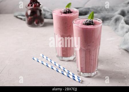 Zwei Portionen selbstgemachte Smoothies mit gefrorenen Brombeeren in hohen Gläsern auf grauem Betongrund, Diät und Gewichtsreduktion Konzept Stockfoto