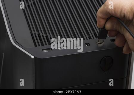 Nahaufnahme des manuellen Anschlusses eines usb-Kabels an einen schwarzen Computer. Stockfoto