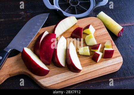 Einen Red Delicious Apple schneiden: Einen roten Apfel auf einem Holzbrett in Stücke schneiden Stockfoto