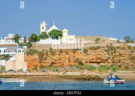 Igreja de Ferragudo (Kirche von Ferragudo) am Ufer des Flusses Arade und einem Fischerboot, gegenüber Portimao, Westalgarve, Südportugal Stockfoto