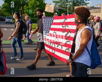 Oak Park, Illinois, USA. Juni 2020. Demonstranten tragen eine amerikanische Flagge, die Gerechtigkeit für George Floyd fordert, einen schwarzen Mann, der von der Polizei getötet wurde. Eine vielfältige Menge von Demonstranten marschierte von der Oak Park Village Hall zur Polizeistation des 15. Bezirks in Chicago und weiter nach Central und Madison. Stockfoto