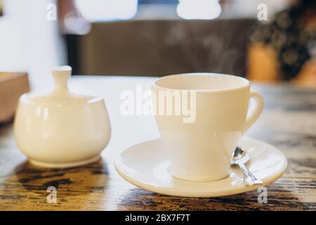 Aromatischer frischer Kaffee in einer weißen Tasse. Espresso in einer kleinen weißen Tasse und eine Zuckerdose in einem Sommercafé. Duftender frischer Kaffee in einem Restaurant Stockfoto