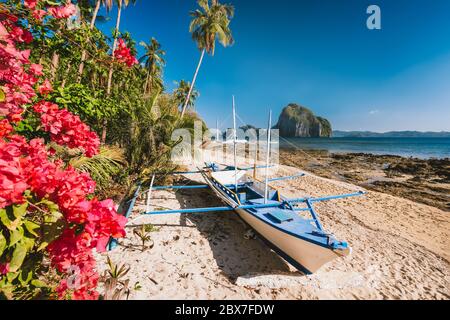 El Nido, Palawan, Philippinen. Native banca Boot und lebendige Blumen am Las Cabanas Strand mit erstaunlichen Pinagbuyutan Insel im Hintergrund Stockfoto