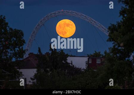 Wembley, Großbritannien. Juni 2020. UK Wetter - der Vollmond im Juni, bekannt als Erdbeermond, erhebt sich hinter dem Wembley Stadion im Nordwesten Londons. Der Vollmond im Juni war laut Almanach des alten Farmers das Signal für die Indianer der Algonquin-Stämme, wilde Erdbeeren zu ernten. Der Vollmond dieses Monats fällt auch mit einer subtilen Halbfinsternis zusammen, die auftritt, wenn die Erde einen leichten Schatten über den Mond wirft. Kredit: Stephen Chung / Alamy Live News Stockfoto