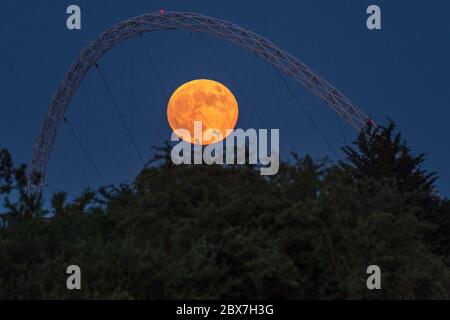 Wembley, Großbritannien. Juni 2020. UK Wetter - der Vollmond im Juni, bekannt als Erdbeermond, erhebt sich hinter dem Wembley Stadion im Nordwesten Londons. Der Vollmond im Juni war laut Almanach des alten Farmers das Signal für die Indianer der Algonquin-Stämme, wilde Erdbeeren zu ernten. Der Vollmond dieses Monats fällt auch mit einer subtilen Halbfinsternis zusammen, die auftritt, wenn die Erde einen leichten Schatten über den Mond wirft. Kredit: Stephen Chung / Alamy Live News Stockfoto