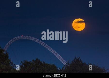 Wembley, Großbritannien. Juni 2020. UK Wetter - der Vollmond im Juni, bekannt als Erdbeermond, erhebt sich hinter dem Wembley Stadion im Nordwesten Londons. Der Vollmond im Juni war laut Almanach des alten Farmers das Signal für die Indianer der Algonquin-Stämme, wilde Erdbeeren zu ernten. Der Vollmond dieses Monats fällt auch mit einer subtilen Halbfinsternis zusammen, die auftritt, wenn die Erde einen leichten Schatten über den Mond wirft. Kredit: Stephen Chung / Alamy Live News Stockfoto