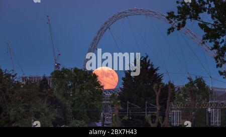 Wembley, Großbritannien. Juni 2020. UK Wetter - der Vollmond im Juni, bekannt als Erdbeermond, erhebt sich hinter dem Wembley Stadion im Nordwesten Londons. Der Vollmond im Juni war laut Almanach des alten Farmers das Signal für die Indianer der Algonquin-Stämme, wilde Erdbeeren zu ernten. Der Vollmond dieses Monats fällt auch mit einer subtilen Halbfinsternis zusammen, die auftritt, wenn die Erde einen leichten Schatten über den Mond wirft. Kredit: Stephen Chung / Alamy Live News Stockfoto