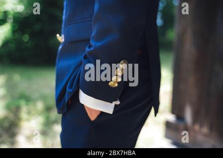 Seitenansicht des Mannes in blauem Anzug mit Hand in der Tasche. Nahaufnahme der Jacke Ärmel goldfarben Knöpfe mit Anker Zeichen. Hintergrund im Freien. Stockfoto