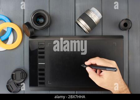 Grafikdesign Grafiktablett und Foto Retusche mit Kameraobjektiven und Farbfiltern. Eine weiße Hand hält den Tablettstift Stockfoto