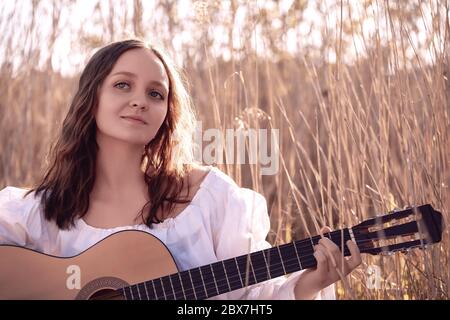 Junge schöne Frau mit langen Haaren Musiker spielen akustische Gitarre bei Sonnenuntergang Feld. Stockfoto