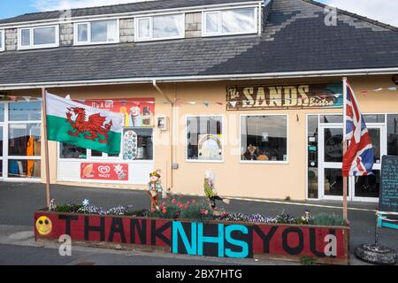 Walisische Flagge, und, Union Jack, Flagge mit Danke NHS, National Health Service, Unterstützung, Poster, Banner, von, Öffentlichkeit, Unterstützung, außerhalb, geschlossen, Sand, Café, Restaurant, dass, ist, geschlossen, aufgrund, Coronavirus, Covid 19, Pandemie, in, Borth, Meer, Urlaub, Resort, Norden, Aberystwyth, Ceredigion hat eine große Anzahl von Einheimischen und Touristen außerhalb Wales zu bleiben. Aber es hat auch eine Wirtschaft mit vielen auf Tourismus, Touristen angewiesen. Stockfoto