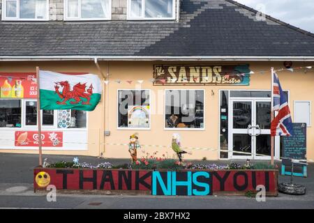 Walisische Flagge, und, Union Jack, Flagge mit Danke NHS, National Health Service, Unterstützung, Poster, Banner, von, Öffentlichkeit, Unterstützung, außerhalb, geschlossen, Sand, Café, Restaurant, dass, ist, geschlossen, aufgrund, Coronavirus, Covid 19, Pandemie, in, Borth, Meer, Urlaub, Resort, Norden, Aberystwyth, Ceredigion hat eine große Anzahl von Einheimischen und Touristen außerhalb Wales zu bleiben. Aber es hat auch eine Wirtschaft mit vielen auf Tourismus, Touristen angewiesen. Stockfoto