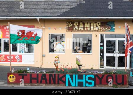 Walisische Flagge, und, Union Jack, Flagge mit Danke NHS, National Health Service, Unterstützung, Poster, Banner, von, Öffentlichkeit, Unterstützung, außerhalb, geschlossen, Sand, Café, Restaurant, dass, ist, geschlossen, aufgrund, Coronavirus, Covid 19, Pandemie, in, Borth, Meer, Urlaub, Resort, Norden, Aberystwyth, Ceredigion hat eine große Anzahl von Einheimischen und Touristen außerhalb Wales zu bleiben. Aber es hat auch eine Wirtschaft mit vielen auf Tourismus, Touristen angewiesen. Stockfoto