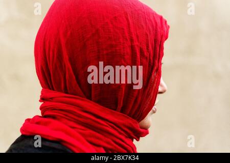 Profil der schönen jungen Frau trägt einen roten Hijab und schwarzen Pullover vor einem neutralen Hintergrund. Diffuses natürliches Licht. Stockfoto