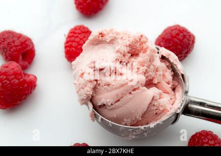 Erfrischende kalte Süßigkeiten, saisonales Dessert und kühles Sommergenuss-Konzept mit einer Kugel leuchtendem Himbeer-Eis und verstreutem Raspel aus nächster Nähe Stockfoto
