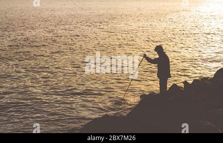 Ein einzelner Mann steht vor einem atemberaubenden Sonnenuntergang und genießt die Schönheit der Natur am Strand beim Angeln Stockfoto