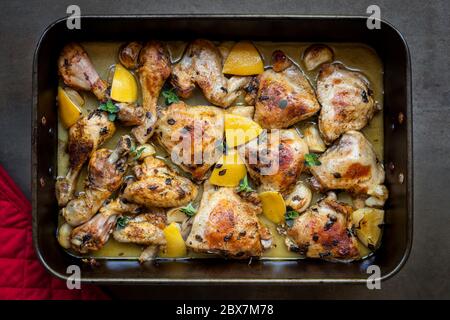 Hähnchen in der Bratpfanne mit Zitrone, Knoblauch und Thymian braten. Blick von oben, auf schwarzem Schiefer. Stockfoto