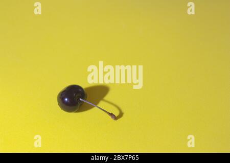 Bild einer Kirsche auf gelbem Hintergrund, die es einen minimalistischen Stil mit Platz für Texte (Kopierraum) gibt Stockfoto