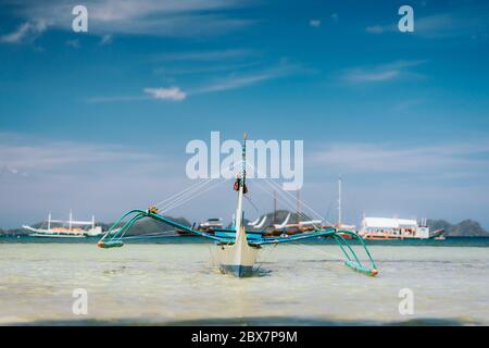 Traditionelles banca-Boot in klarem Wasser am Sandstrand von Corong Beach in El Nido, Philippinen. Ansicht mit niedrigem Winkel Stockfoto
