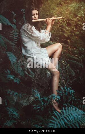 Schöne Trockenhaut spielt eine Flöte im Wald. Romantik und Fantasie Stockfoto