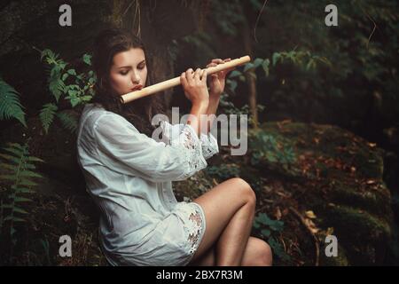 Schöne Frau spielt Flöte nach dem Regen in einem Wald. Romantik und Fantasie Stockfoto