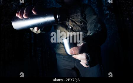 Camping Mann in der Nacht Wald Ausgießen Wasser aus Thermoskannen in einer Tasse. Stockfoto