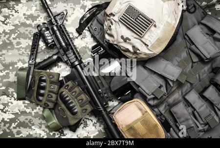 Foto einer taktischen Weste, Gewehr, Pistole, Hut mit amerikanischer Flagge Abzeichen und cartrige Gürtel auf Tarnhintergrund. Stockfoto