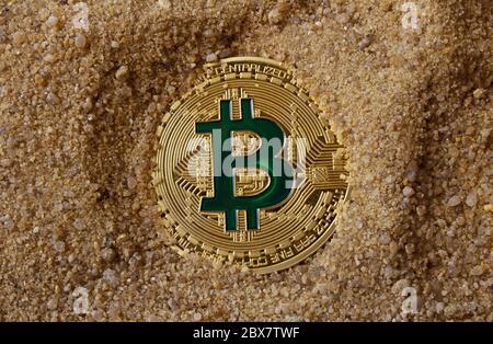 Foto einer goldenen Bitcoin Münze, die im Sand liegt. Stockfoto