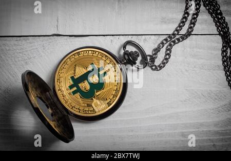 Foto einer altmodischen, geöffneten Bitcoin-Uhr, die auf einer weißen Tischfläche aus Holz liegt. Stockfoto