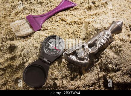 Archäologiebürste & Kompass auf einem Sand neben pharao Metallstatuette. Stockfoto