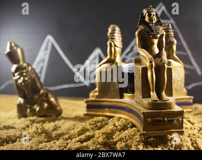 Alte alte Metallstatuetten stehen auf einer Sandfläche mit einer Tafel gezeichneter Hintergrund. Stockfoto