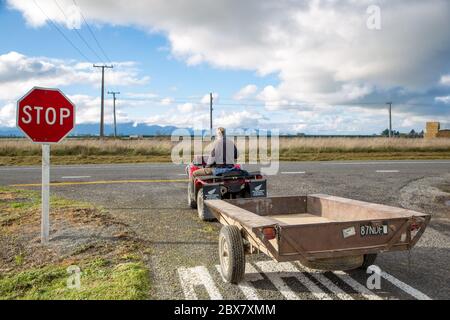 Annat, Canterbury, Neuseeland, Mai 26 2020: Ein pensionierter Bauer schleppen einen Anhänger hinter sein Quad und halten an einem Give Way Schild auf einer Landstraße