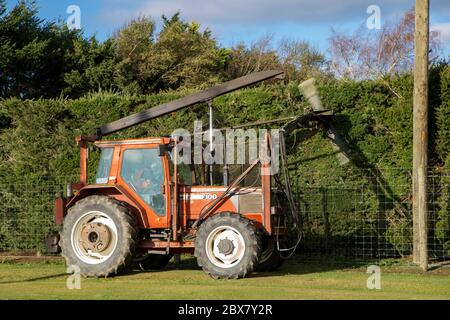 Annat, Canterbury, Neuseeland, Mai 26 2020: Ein Traktor mit einer montierten Heckenschere trimmt entlang einer Grenzstraße, einem Zaun und um einen Mast Stockfoto