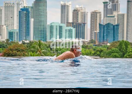 Ein Mann schwimmt einen Schmetterling in einem Pool auf dem Dach eines Luxushotels. Blick auf die Stadt Manila vom Pool des luxuriösen Fünf-Sterne-Discovery Primea Hot Stockfoto