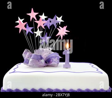 Torte mit Kerze Nummer eins. Mit Bändern und Sternformen dekoriert, in Pastelltönen auf schwarzem Hintergrund. Stockfoto