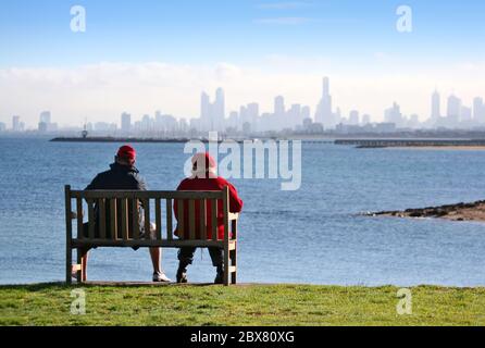 Ein Mann und eine Frau auf einer Clifftop Bank genießen den Blick über die Bucht auf die Skyline der Stadt. Melbourne, Australien, im frühen Morgenlicht. Stockfoto