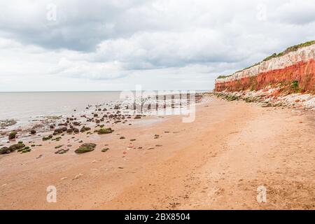 Orangene, rote und weiße Sedimentgesteine am Strand in Hunstanton, Norfolk, East Anglia, Großbritannien. Stockfoto